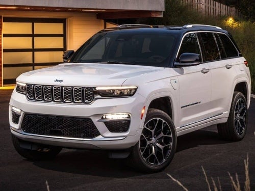 2024 Jeep Grand Cherokee parked outside a modern building at night with headlights on